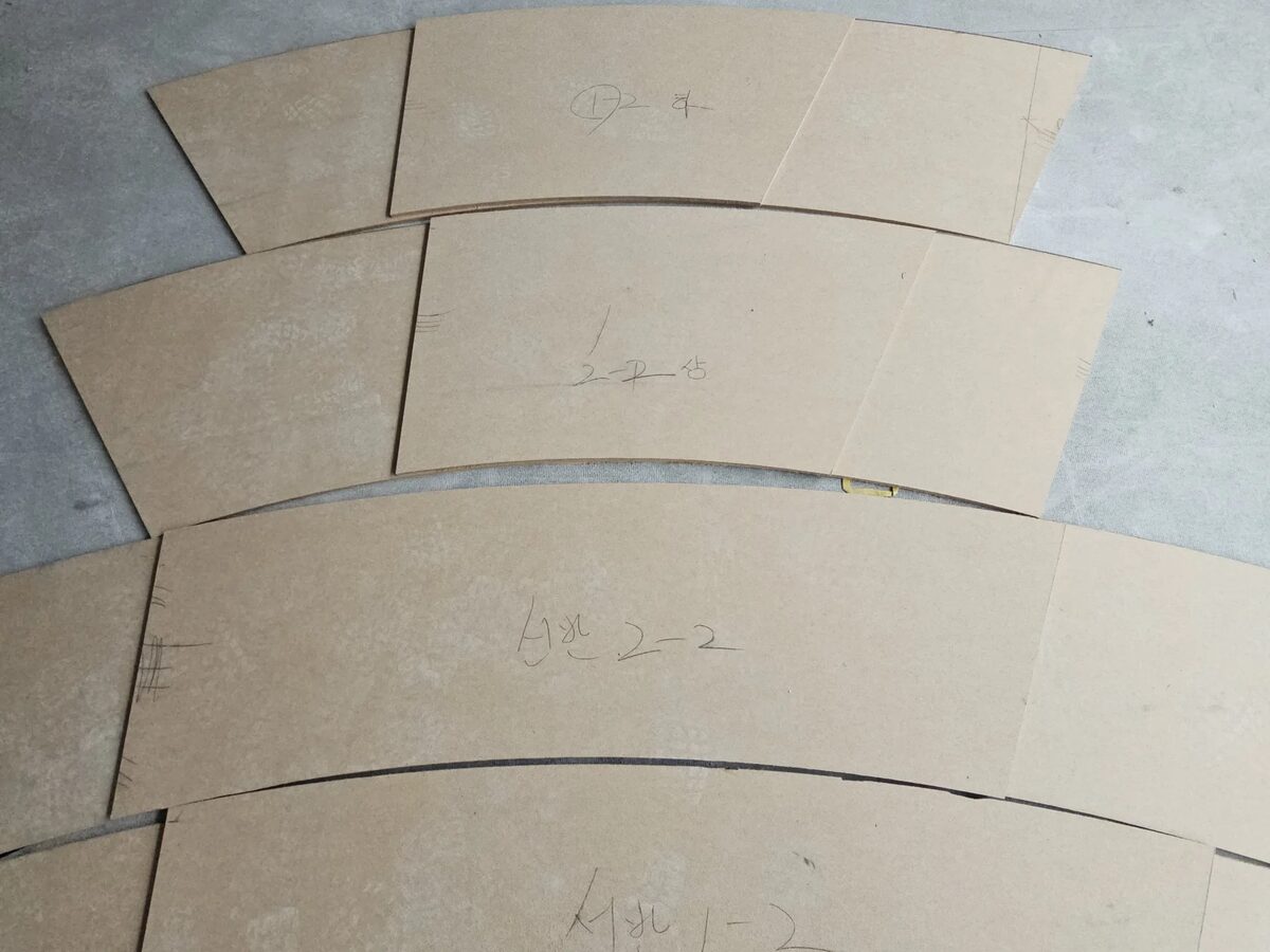 원형 곡면몰딩용으로 재단된 곡선 부재 조각들이 곡률 템플릿과 함께 바닥에 정렬된 모습